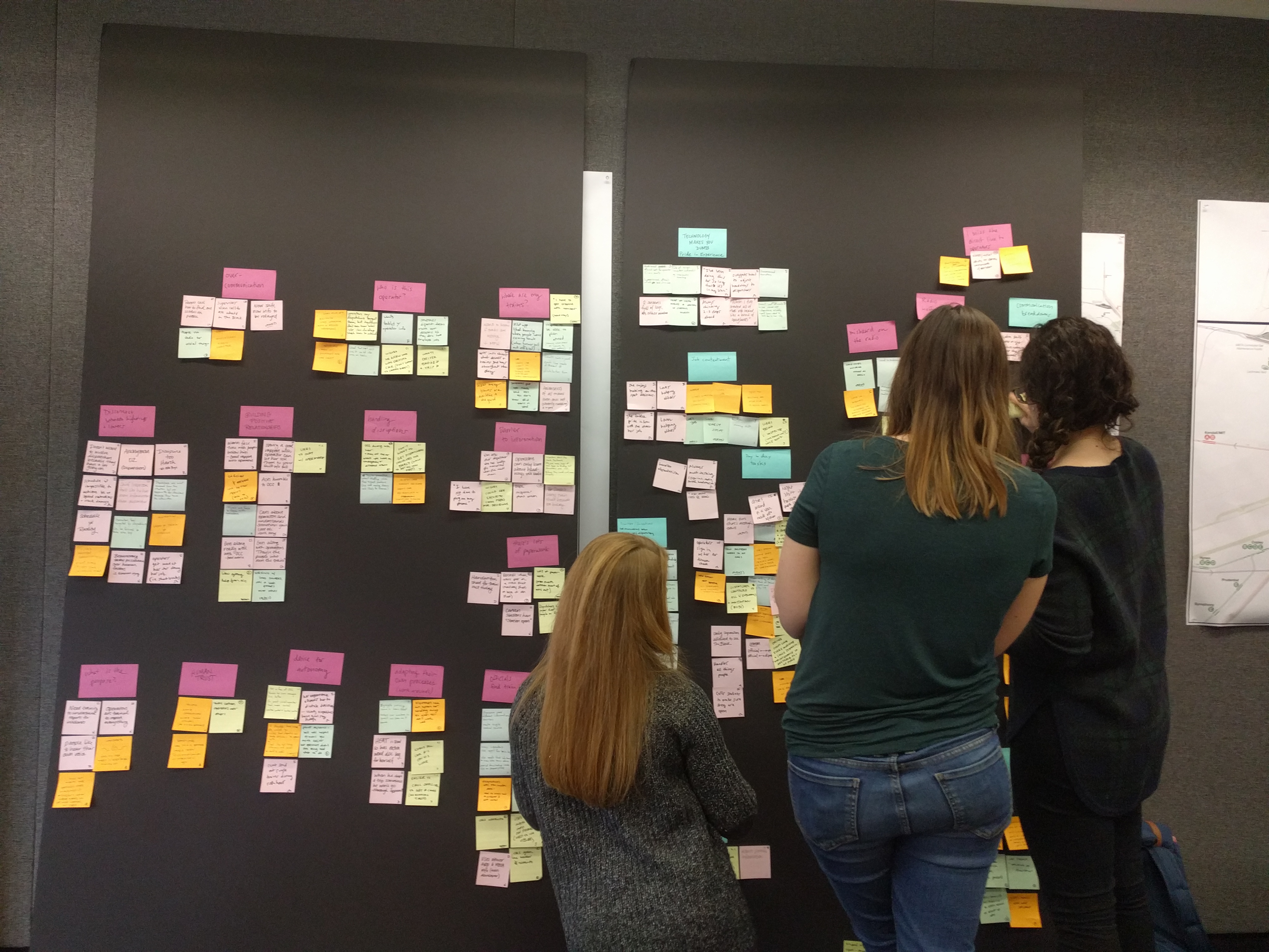 Three women in front of a large wall full of post-it notes